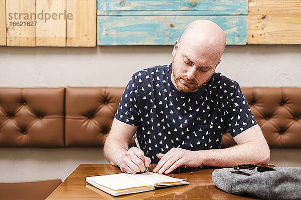 Mittlerer erwachsener Mann  der in einem Café sitzt und in ein Notizbuch schreibt