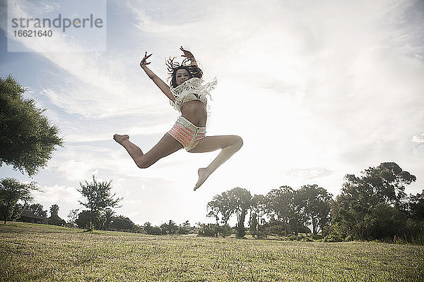 Junge Frau springt gegen den klaren Himmel in einem öffentlichen Park