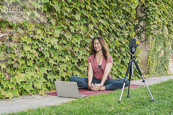 Yogalehrer unterrichtet Yoga in einem Online-Yogakurs mit Mobiltelefon und Laptop