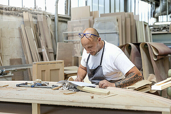 Zimmermann liest Entwurf in Papier  während er an einer Werkbank in einer Fabrik steht