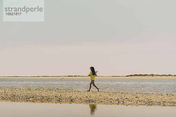 Mädchen läuft am Strand gegen den Himmel an einem sonnigen Tag