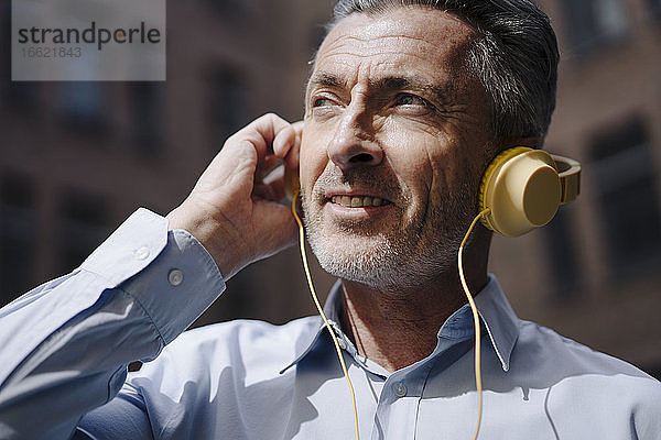 Geschäftsmann mit Kopfhörern hört Musik  während er vor einem Gebäude steht