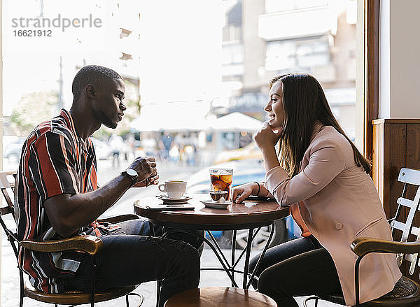 Lächelnde junge Frau im Gespräch mit ihrem Freund  während sie ihre Freizeit in einem Café verbringt