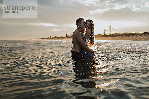 Mann küsst Frau  während er am Strand im Wasser steht