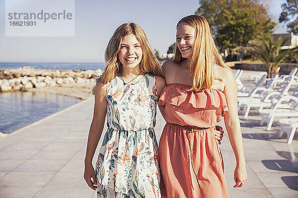 Lächelnde Mädchen stehen auf dem Bürgersteig gegen das Meer an einem sonnigen Tag