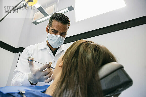 Ein männlicher Zahnarzt betäubt eine Patientin vor einer Zahnbehandlung in einer Klinik