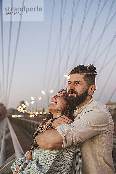 Freund umarmt glückliche Freundin  während er auf einer Brücke in der Stadt steht