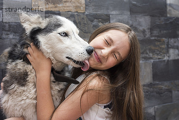 Mädchen umarmt Hund und sitzt an der Wand