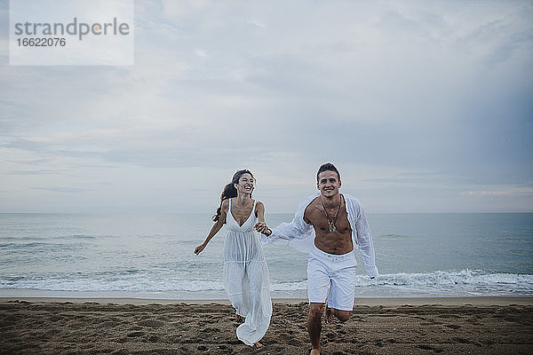 Glückliches Paar hält sich beim Laufen am Strand an den Händen