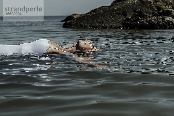 Ältere Frau mit geschlossenen Augen schwimmt auf dem Meer an einem sonnigen Tag