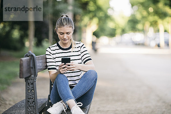 Mittlere erwachsene Frau  die ein Smartphone benutzt  während sie in einem öffentlichen Park sitzt