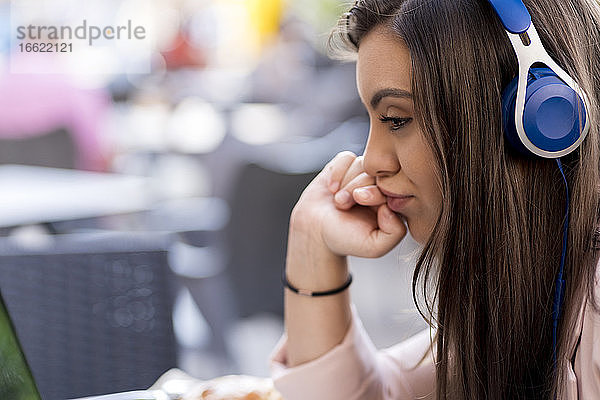Nachdenkliche Geschäftsfrau mit Kopfhörern  während sie im Café sitzt