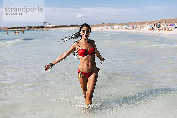 Fröhlich Mitte erwachsene Frau trägt Bikini zu Fuß im Meer gegen den Himmel