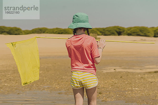 Mädchen mit gelbem Fischernetz am Strand stehend an einem sonnigen Tag