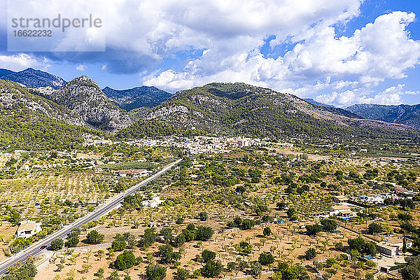 Luftaufnahme einer Straße in Richtung eines Dorfes in der Nähe einer Gebirgskette bei bewölktem Himmel  Caimari  Mallorca  Spanien