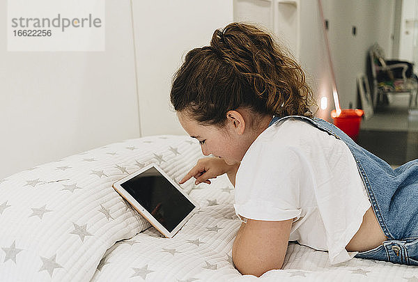 Mädchen  das ein digitales Tablet benutzt  während es zu Hause auf dem Bett liegt