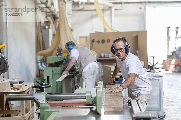 Mitarbeiter tragen Ohrenschützer beim Sägen von Holz in einer Maschine in einer Fabrik