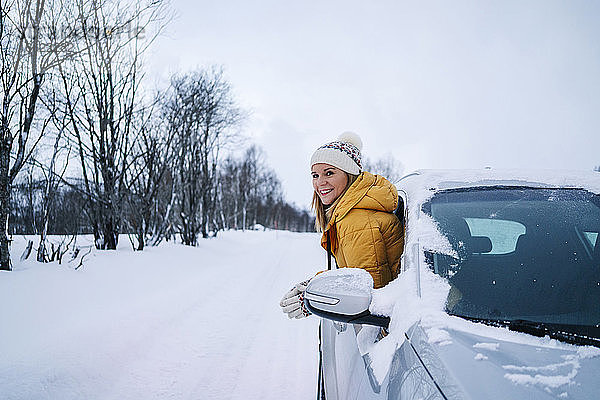 Lächelnde Frau  die durch ein Autofenster gegen den Winterhimmel blickt