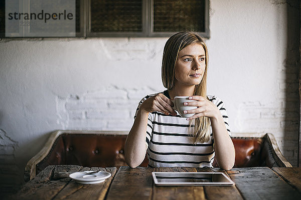 Frau schaut weg und trinkt eine Tasse Kaffee  während sie in einem Cafe sitzt