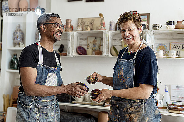 Lächelnde Künstler  die Keramik in der Hand halten  während sie in der Werkstatt stehen
