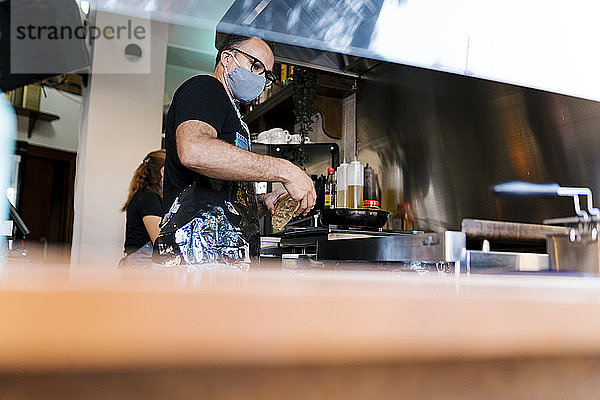 Männlicher Barista mit Gesichtsschutz beim Kochen in der Küche einer Kaffeebar während COVID-19