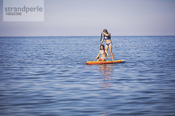 Freunde surfen auf einem Stand Up Paddle Board im Meer an einem sonnigen Tag