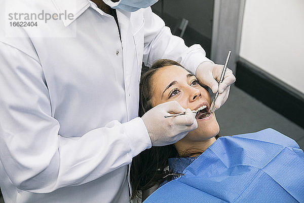 Männlicher Zahnarzt inspiziert die Mundhöhle einer jungen Patientin in der Klinik