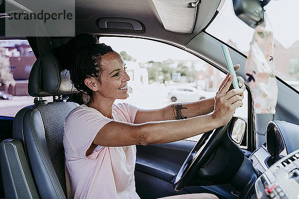 Lächelnde Frau  die ein Selfie macht  während sie an einem sonnigen Tag im Auto sitzt