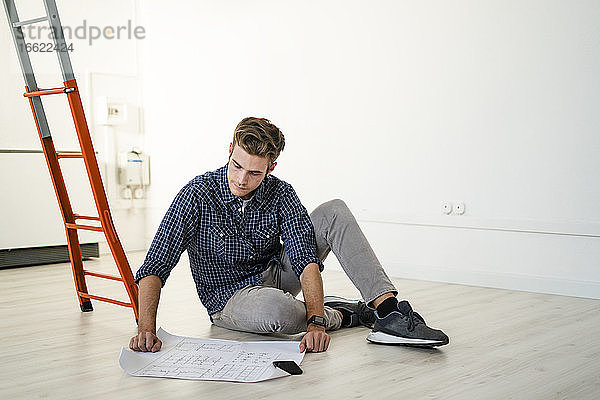Architekt auf dem Boden sitzend beim Lesen eines Bauplans im Büro