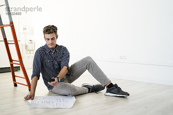 Architekt  der einen Bauplan fotografiert  während er im Büro auf dem Boden sitzt