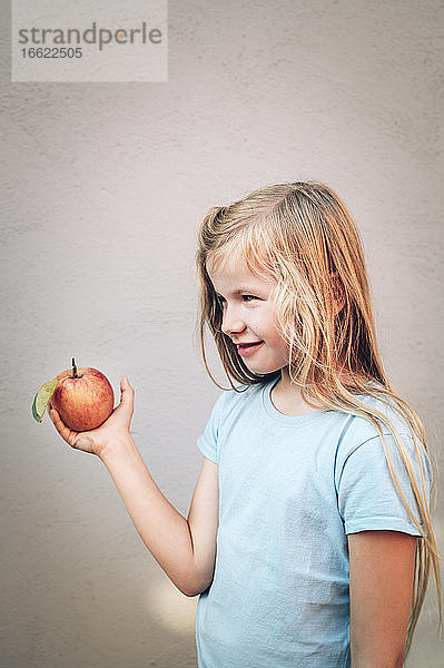 Nettes blondes Mädchen hält frischen roten Bio-Apfel an der Wand