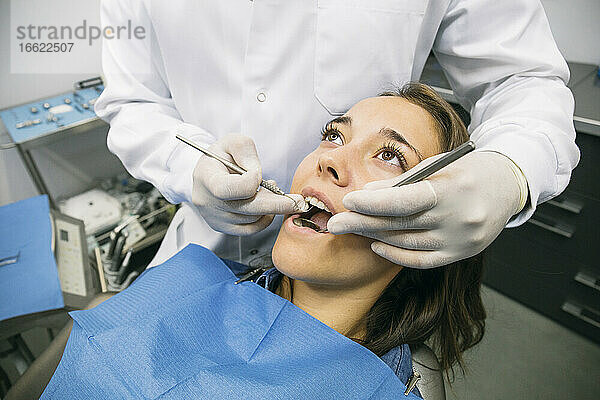 Männlicher Zahnarzt in Handschuhen untersucht die Mundhöhle einer hübschen Patientin in einer Klinik