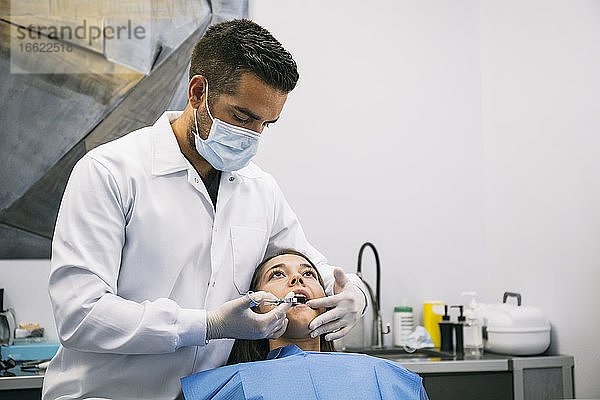 Ein männlicher Zahnarzt betäubt eine junge Patientin vor einer Zahnbehandlung in einer Klinik