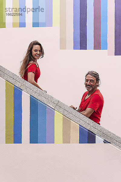 Lächelnder Vater und Tochter stehen auf einer bunten Treppe an einem sonnigen Tag