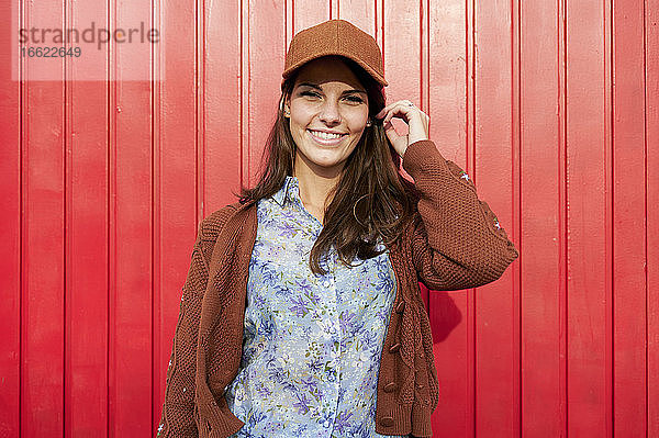 Lächelnde Frau mit Hut  die vor einer roten Metalltür steht