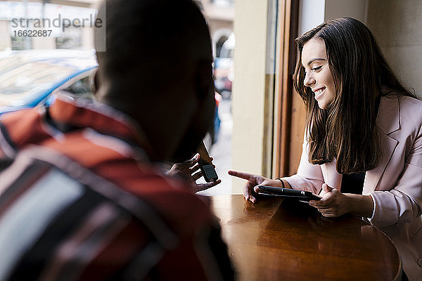 Junger Mann zeigt seiner Freundin das Smartphone  während er im Café sitzt