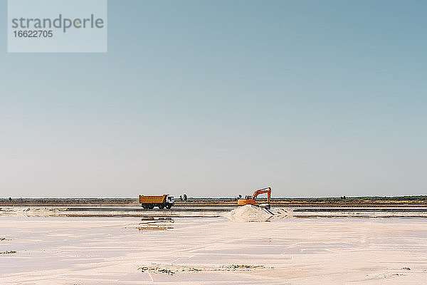 Spanien  Provinz Huelva  Huelva  Klarer Himmel über Lkw und Erdbewegungsmaschine bei der Arbeit im Salzsee