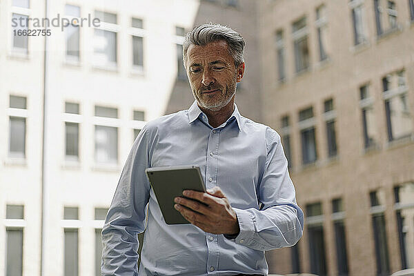 Geschäftsmann  der ein digitales Tablet benutzt  während er an einem Gebäude steht