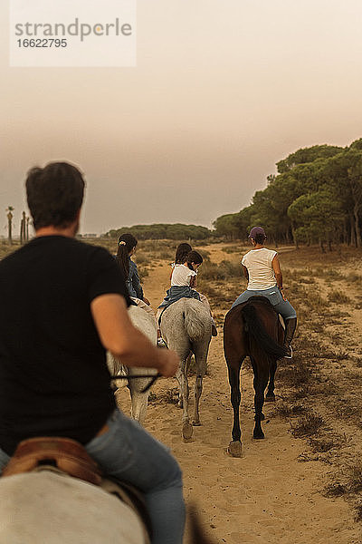 Familie reitet Pferde auf Landschaft gegen klaren Himmel bei Sonnenuntergang