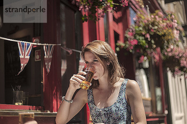 Frau trinkt Bier  während sie an einem sonnigen Tag vor einer Kneipe sitzt