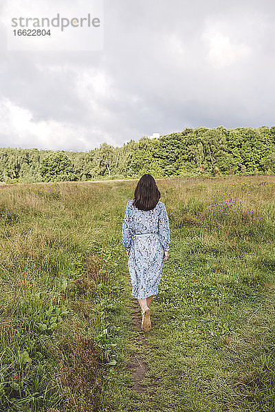 Mid erwachsene Frau zu Fuß auf grasbewachsenen Land gegen bewölkten Himmel