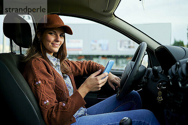 Lächelnde junge Frau  die ein Mobiltelefon benutzt  während sie im Auto sitzt