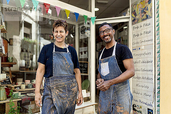 Lächelnde Mitarbeiter mit Schürzen stehen vor einem Keramikgeschäft