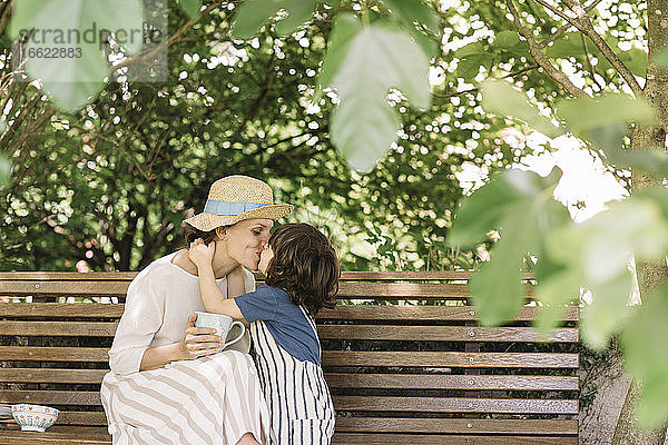 Sohn küsst seine Mutter auf einer Bank im Hinterhof sitzend