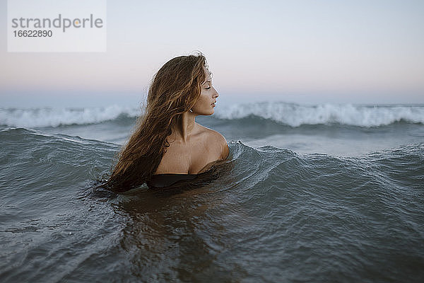 Schöne junge Frau im Meer am Strand bei Sonnenuntergang