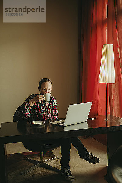 Geschäftsfrau trinkt Kaffee und arbeitet am Laptop im Büro
