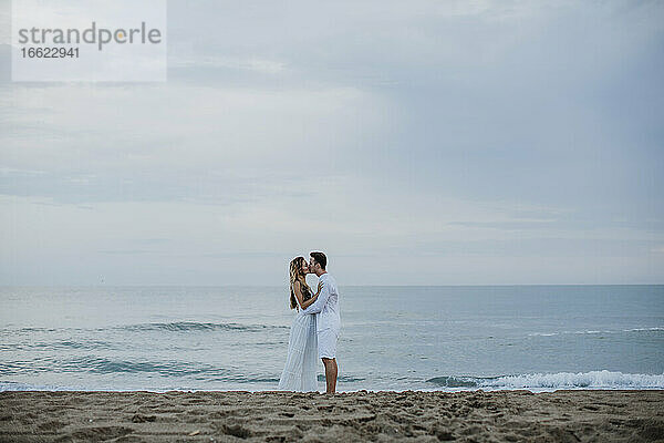 Paar küsst sich  während es am Strand am Meer steht