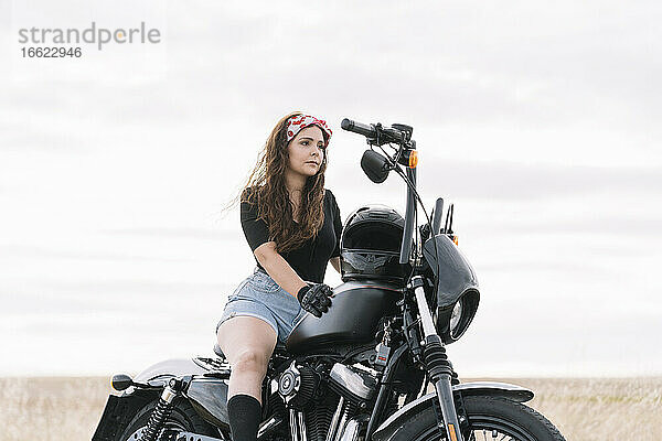 Junge Frau auf Motorrad sitzend gegen den Himmel