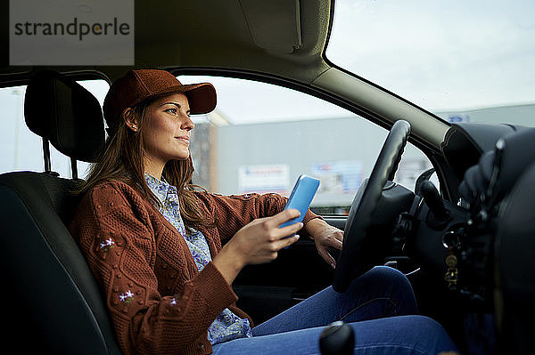 Junge Frau  die im Auto sitzend ein Mobiltelefon benutzt