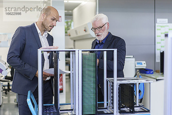 Ein leitender Angestellter diskutiert mit einem Kollegen in einer Fabrik über Maschinen